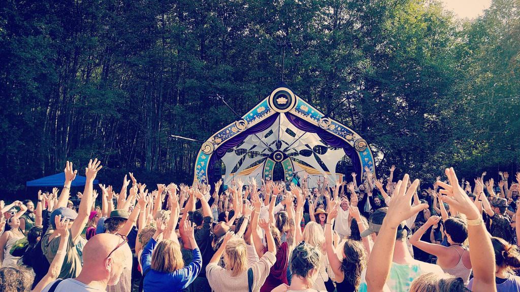 What’s all this Spirituality stuff about, and can I do it too …? 1 Festival crowd raising their hands toward a decorated woodland stage.