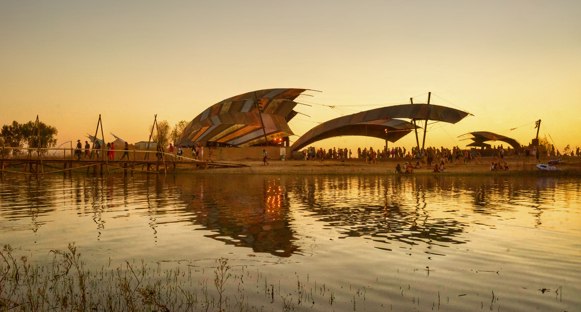 The History of Music Festivals 1 Festival stages and crowds reflected in a lake at sunset.